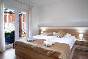 Ein Hotelzimmer mit Bett, Nachttisch, Fenster mit Vorhängen und Blick auf einen Außenbereich.