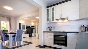 Una cocina moderna con armarios blancos, un comedor con mesa y sillas, y un horno visible.