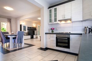 Eine moderne Küche mit weißen Schränken, ein Essbereich mit Tisch und Stühlen sowie ein sichtbarer Backofen.