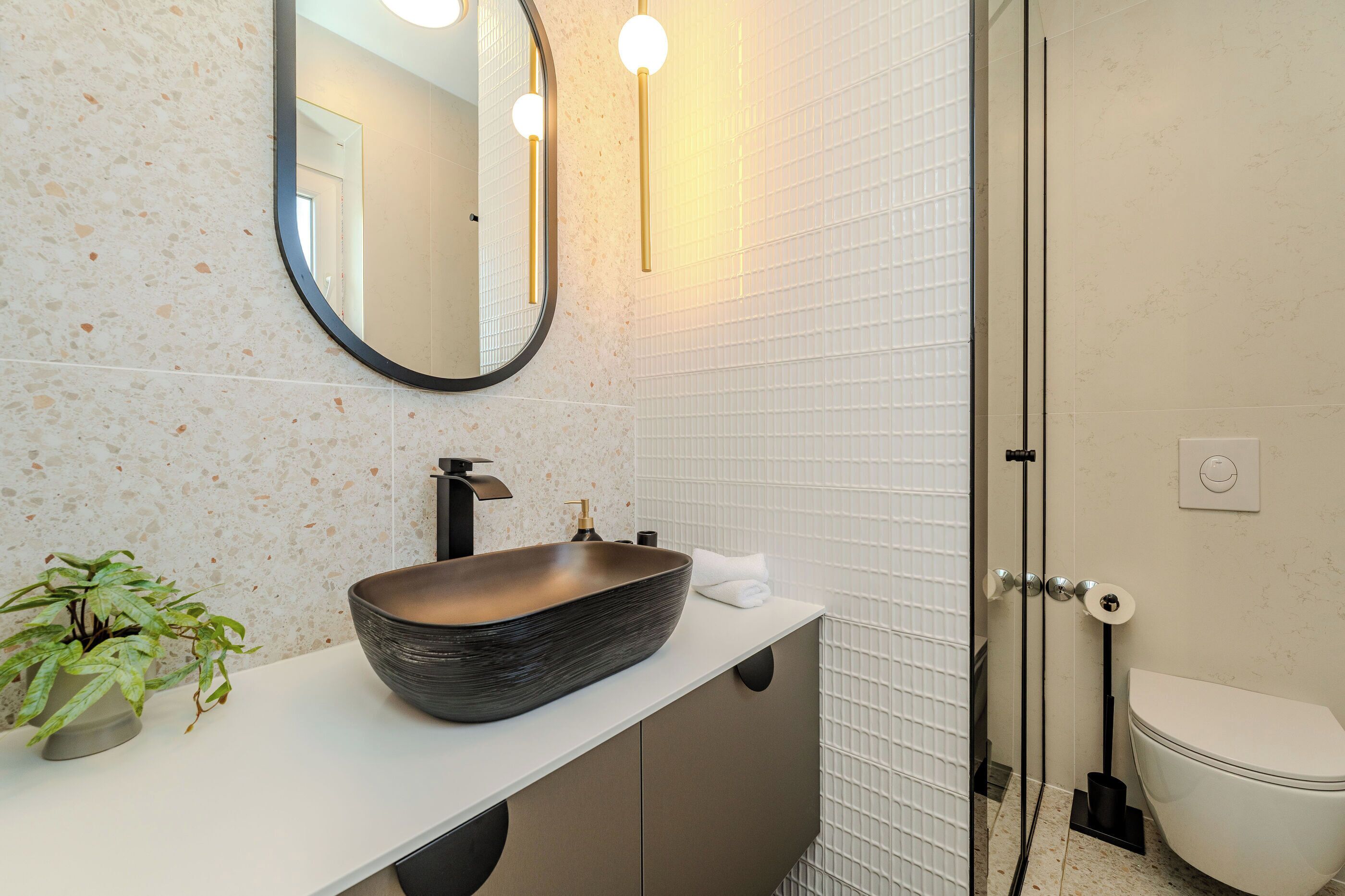 Une salle de bain avec un lavabo sur colonne, une plante en pot, un miroir et des toilettes.