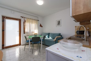 A compact living space with a dining area, a sofa, a kitchen with a microwave, and a large window with curtains. - Apartment Mary (Punat)