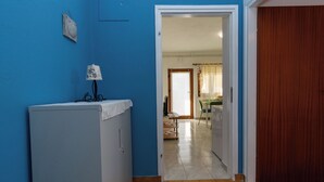 A room with a blue wall, a white cabinet, a wooden door, and a view into a dining area. - Apartment Mary (Punat)