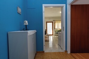A room with a blue wall, a white cabinet, a wooden door, and a view into a dining area. - Apartment Mary (Punat)
