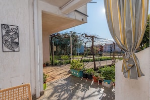 A covered outdoor area with potted plants, a metal trellis, and a woven chair. - Apartment Mary (Punat)