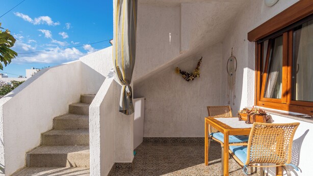 A covered outdoor area with a staircase, a table with chairs, and a decorative wall piece. - Apartment Mary (Punat)