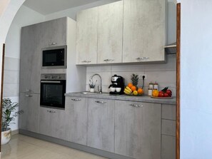 A modern kitchen with grey cabinetry, a built-in oven, microwave, and coffee maker.