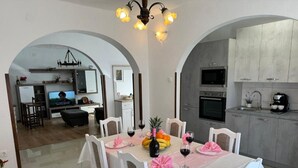 A dining area with a table set for four, a kitchen with modern appliances, and an arched doorway leading to another room. - House Relax Residence (Liznjan)