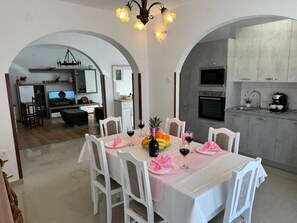 A dining area with a table set for four, a kitchen with modern appliances, and an arched doorway leading to another room.