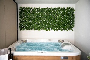 A hot tub with water, a wooden cabinet, and a wall with green foliage. - Mobile Home Aura With Jacuzzi (Vodice)