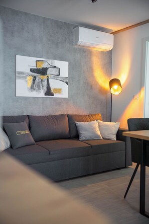 A modern living room with a grey sofa, a painting, a standing lamp, and an air conditioning unit. - Mobile Home Aura With Jacuzzi (Vodice)