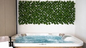 Um banheiro moderno com uma banheira de madeira, um degrau para facilitar o acesso e um painel decorativo com folhagem verde.