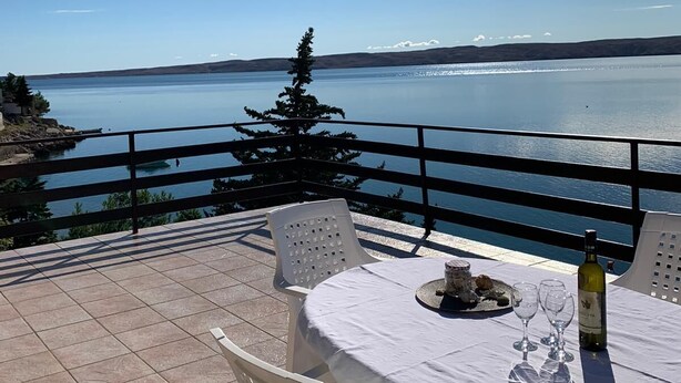 A terrace with a table set for two, overlooking a body of water and distant hills. - Apartment Nada (Karlobag)