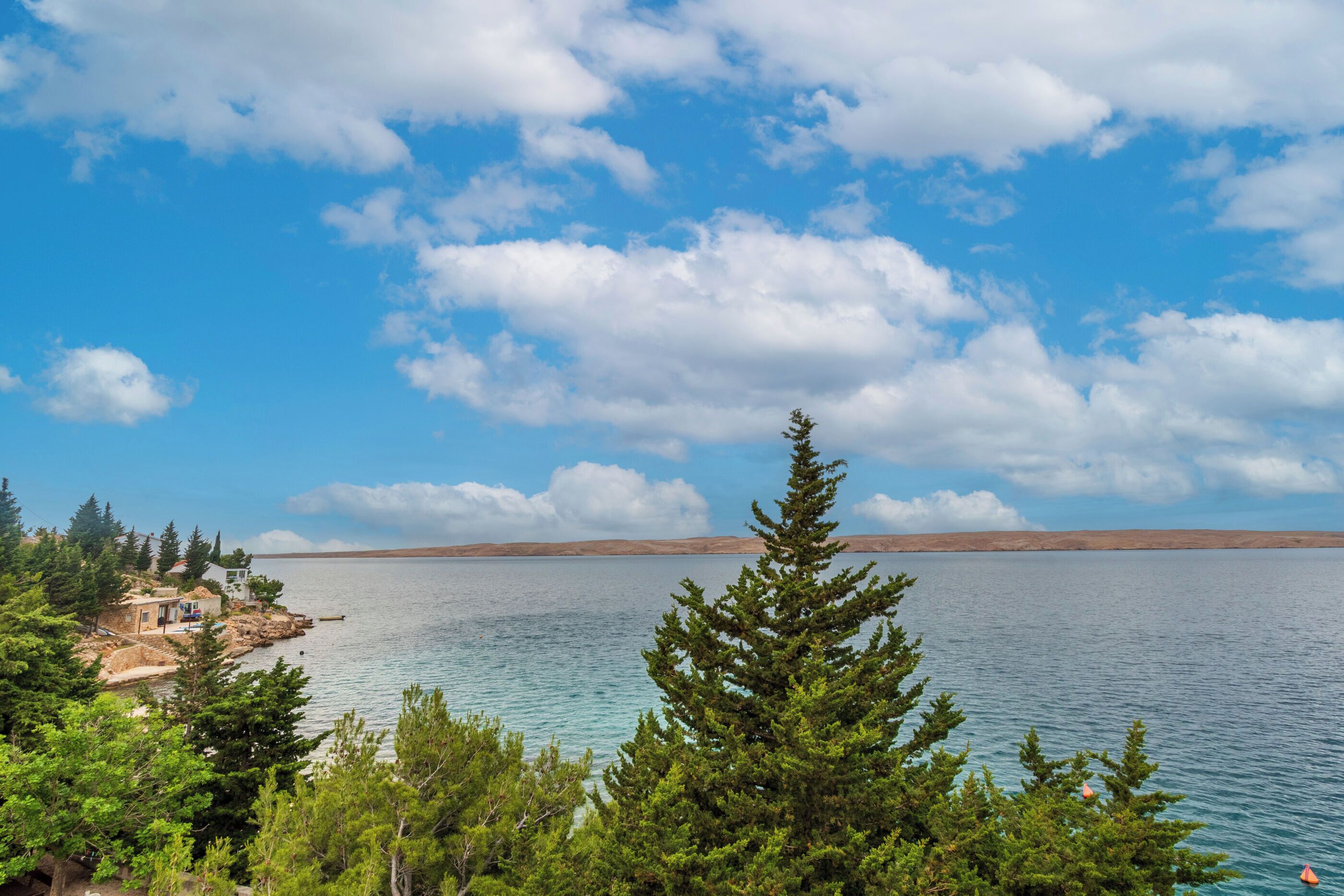 A lake with a house on a rocky shore, surrounded by trees.