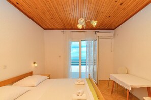 Ein Schlafzimmer mit Holzbalkendecke, einem Bett mit Kissen, einem Nachttisch, einem Stuhl und Blick durch ein Fenster.