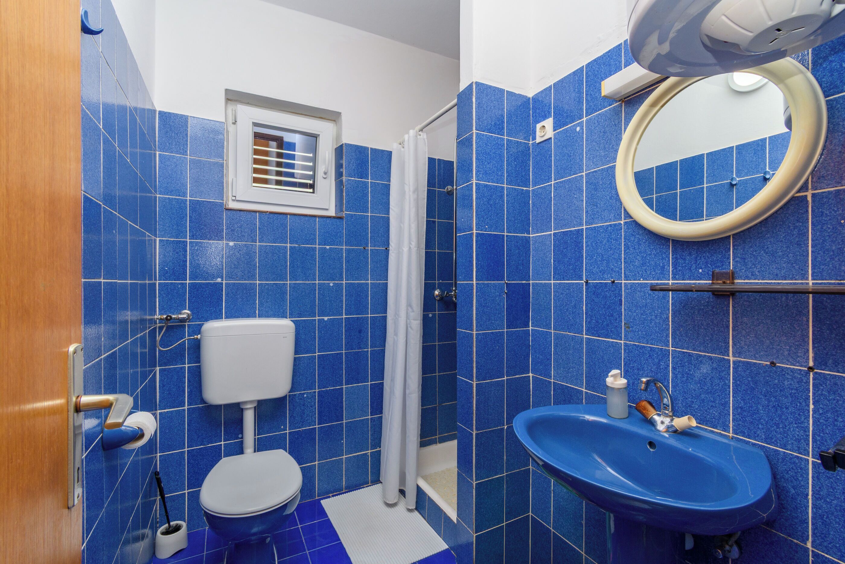A bathroom with blue tiles, a white toilet, a blue sink, a shower curtain, and a mirror.