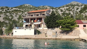 A coastal building with a balcony, a stone wall, and a mountain in the background. - Apartment Nada (Karlobag)