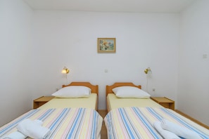 Ein Doppelzimmer mit zwei Betten, jeweils mit Holz Kopfteil, weißen Kissen und gestreifter Bettwäsche. Es gibt Nachttischlampen und ein gerahmtes Bild an der Wand.