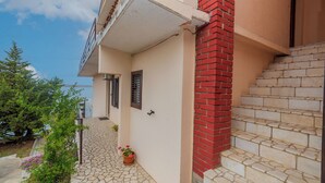 A building with a stone-paved entrance, a red brick staircase, and a small potted plant. - Apartment Nada (Karlobag)