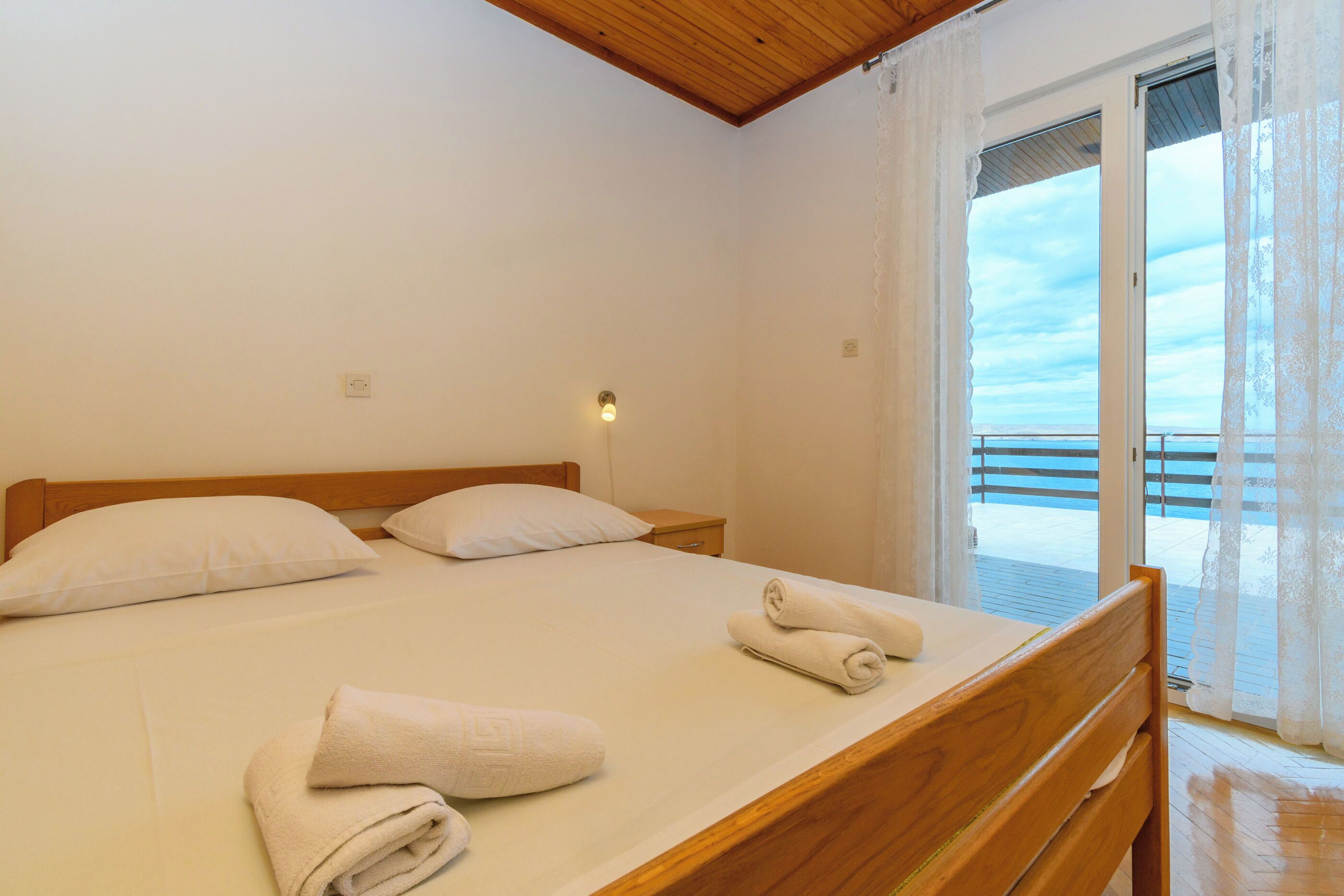 Un dormitorio con cama de madera, ropa de cama blanca y vista al mar desde un balcón.