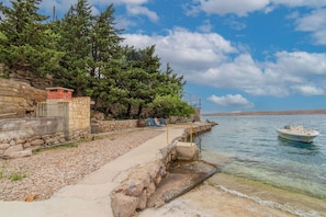 Ein Steinweg führt zu einem Gewässer, ein kleines Boot liegt angedockt und der Himmel ist wolkenlos.