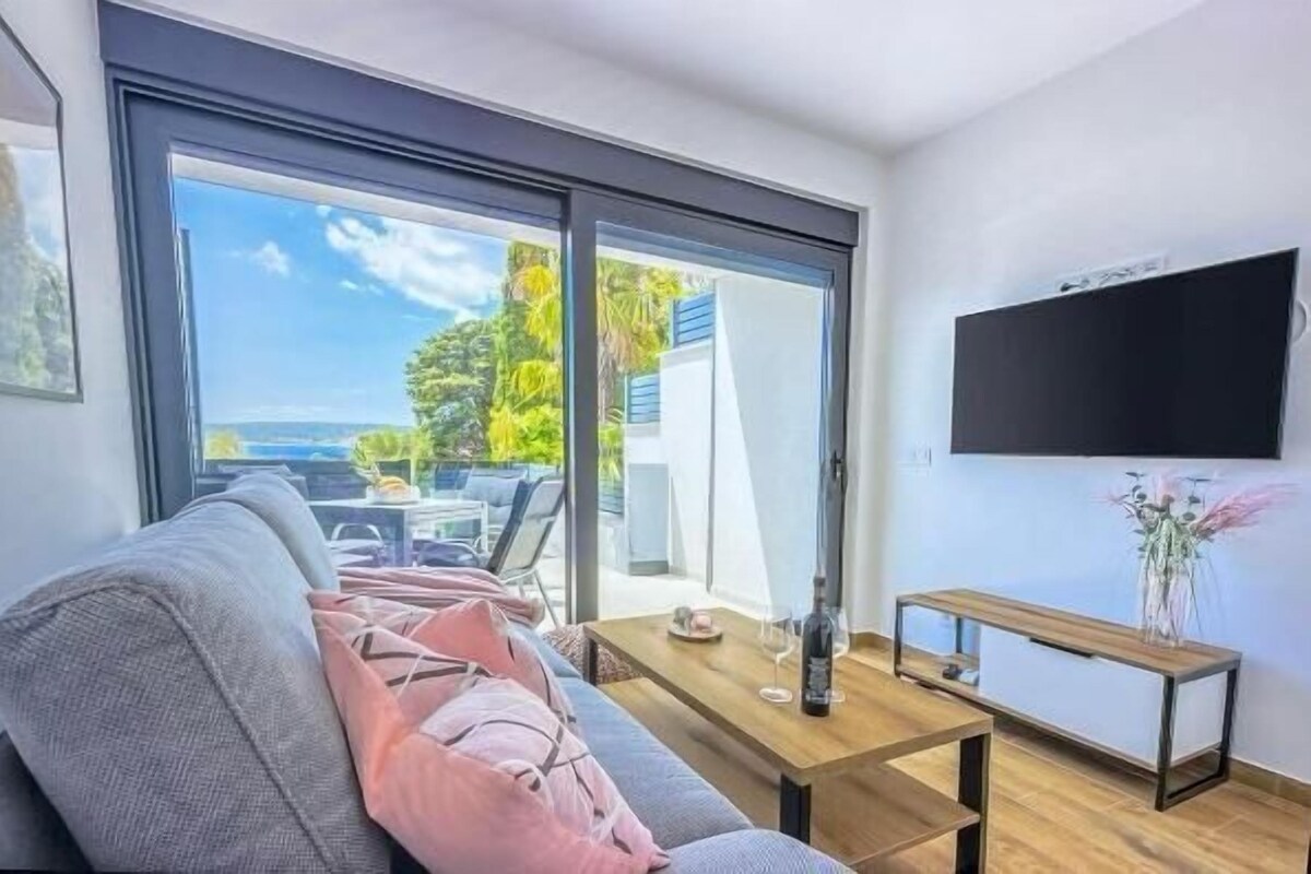 A modern living room with a sofa, a coffee table, a TV mounted on the wall, and a sliding glass door leading to an outdoor area.