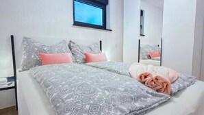 A double bed with patterned bedding, a bedside table, a window, and a mirror. - Apartments Sladana (Crikvenica)