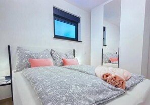 A double bed with patterned bedding, a bedside table, a window, and a mirror. - Apartments Sladana (Crikvenica)