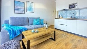 A modern living room with a sofa, a coffee table, and a kitchen area with a microwave. - Apartments Sladana (Crikvenica)