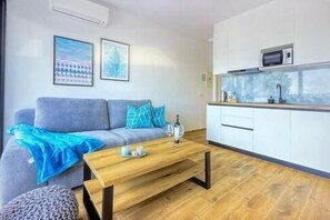 A modern living room with a sofa, a coffee table, and a kitchen area with a microwave. - Apartments Sladana (Crikvenica)