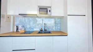 A compact kitchen with white cabinets, a microwave, a sink, and a coffee maker. - Apartments Sladana (Crikvenica)