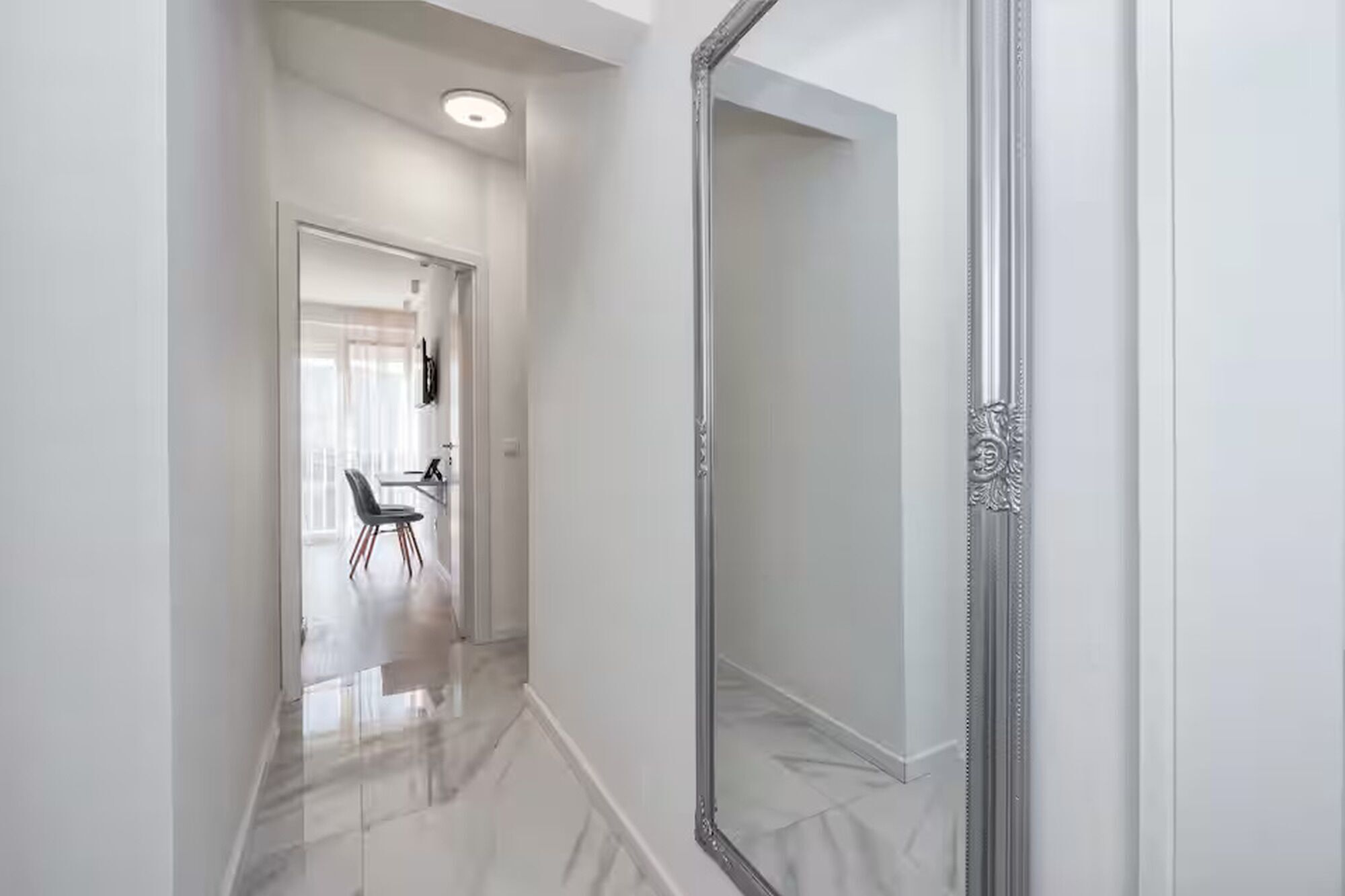 Un pasillo con una puerta espejo de armario, una zona de comedor con una mesa y sillas, e iluminación en el techo.