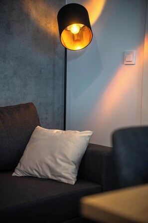 A modern living room with a dark sofa, a white pillow, and a floor lamp casting a warm glow. - Mobile Home Aria With Jacuzzi (Vodice)