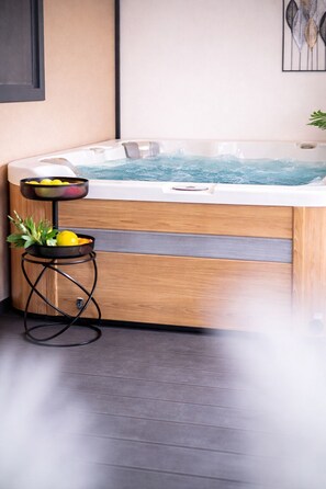 Ein Whirlpool mit einer Holzbank, einem kleinen Tisch mit Zitronen und einer Pflanze, sowie einem an der Wand befestigten Kunstwerk.