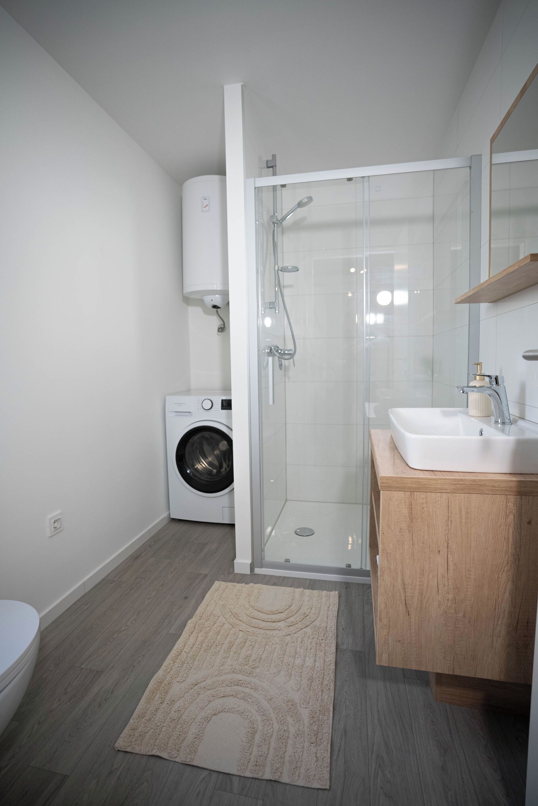 A modern bathroom with a glass shower enclosure, a washing machine, and a wooden vanity.