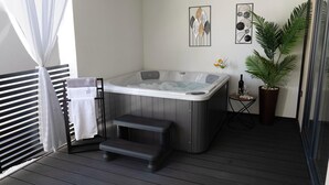 Ein Wellnessbereich mit Whirlpool, Handtuchhalter, einem kleinen Tisch mit Flasche und Glas sowie einer Topfpflanze.