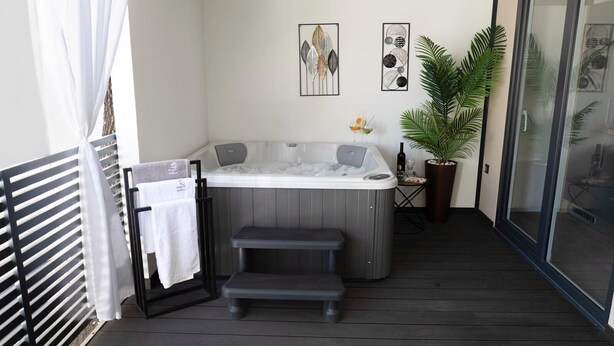 Ein Whirlpool auf einer Holzdielen-Terrasse mit Handtuchhalter und einer Topfpflanze.