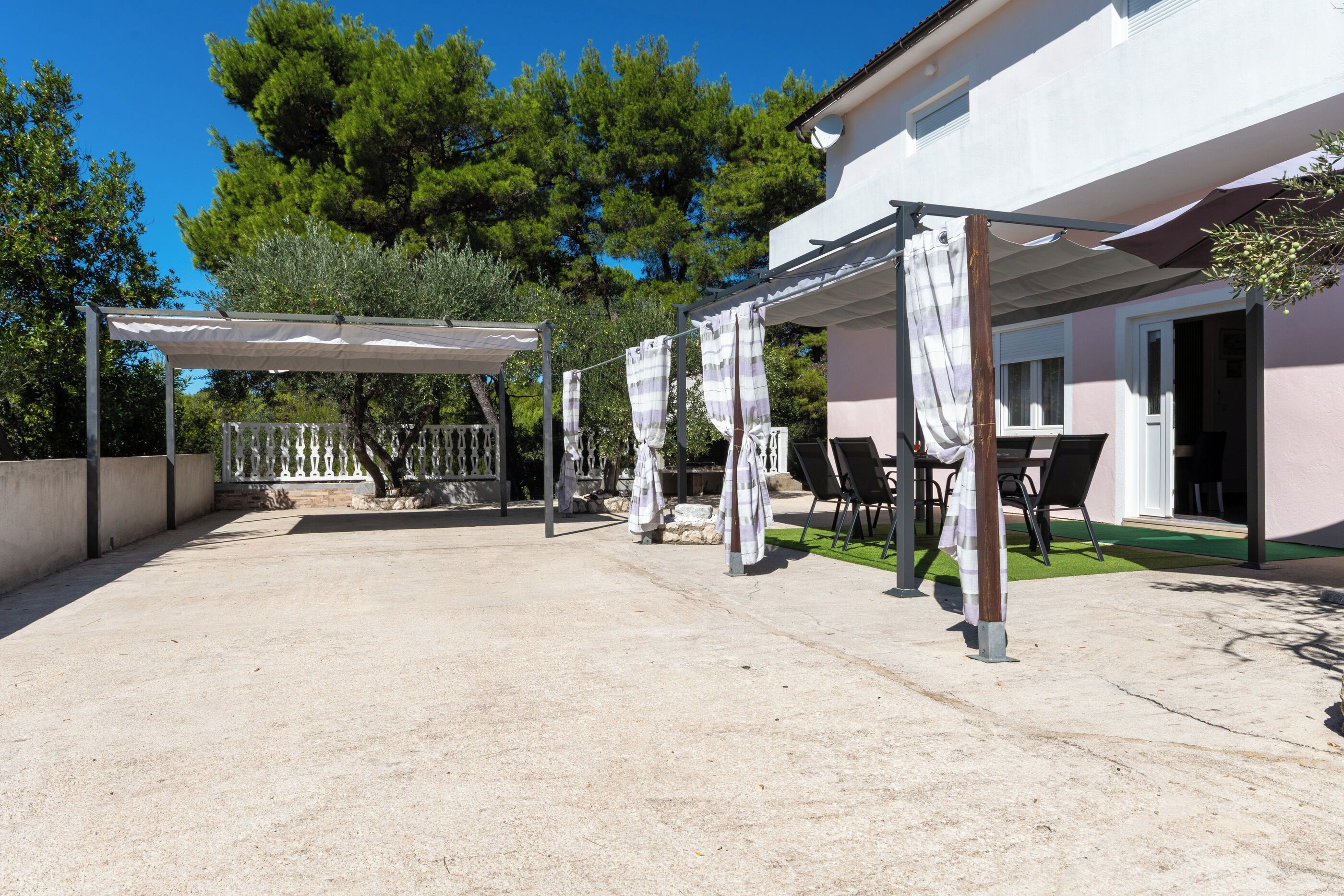 Un espacio de estar al aire libre cubierto con mesas y sillas, una pérgola y un edificio de fachada blanca.