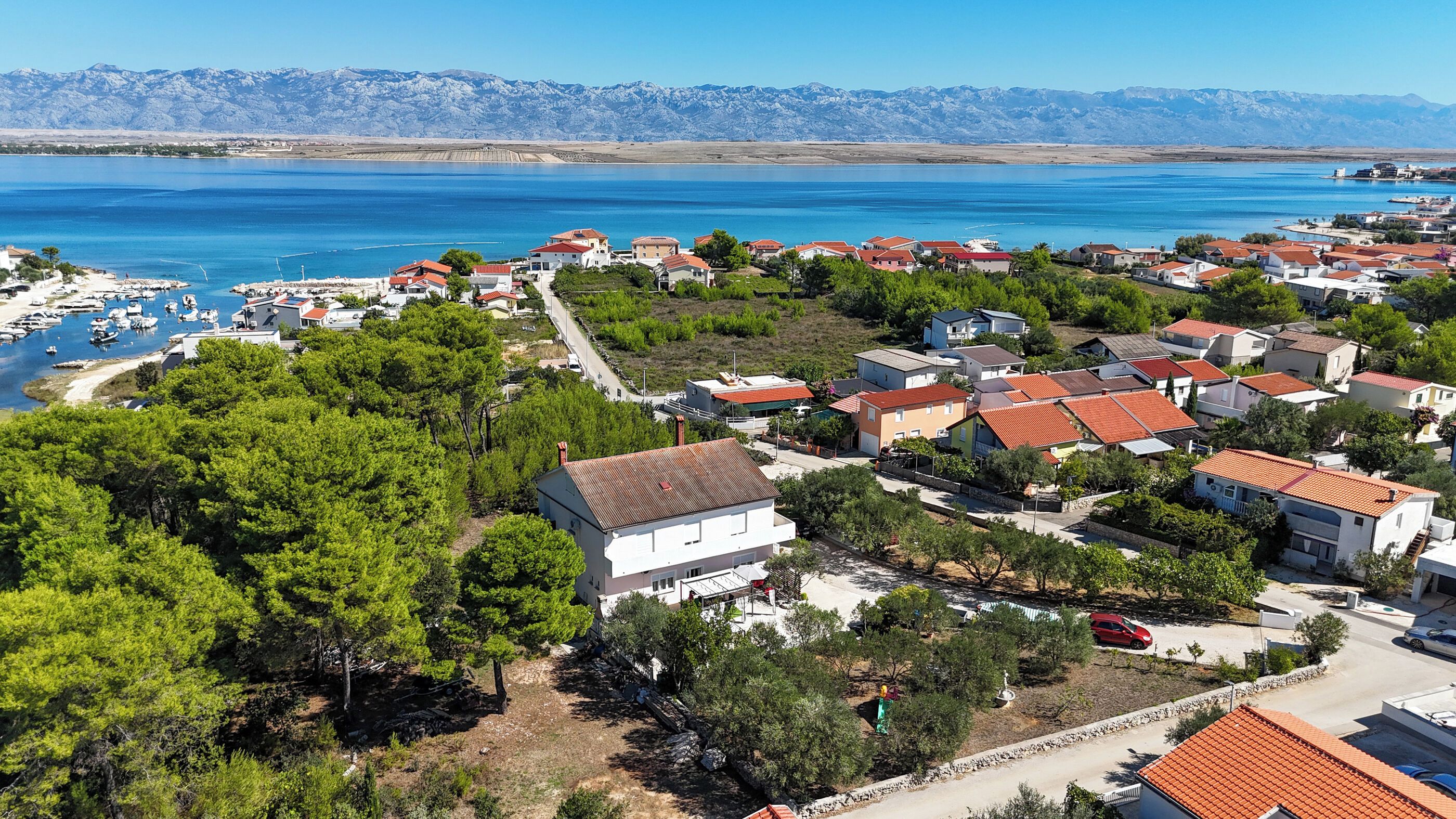 A coastal residential area with houses, a marina, and mountains in the background.