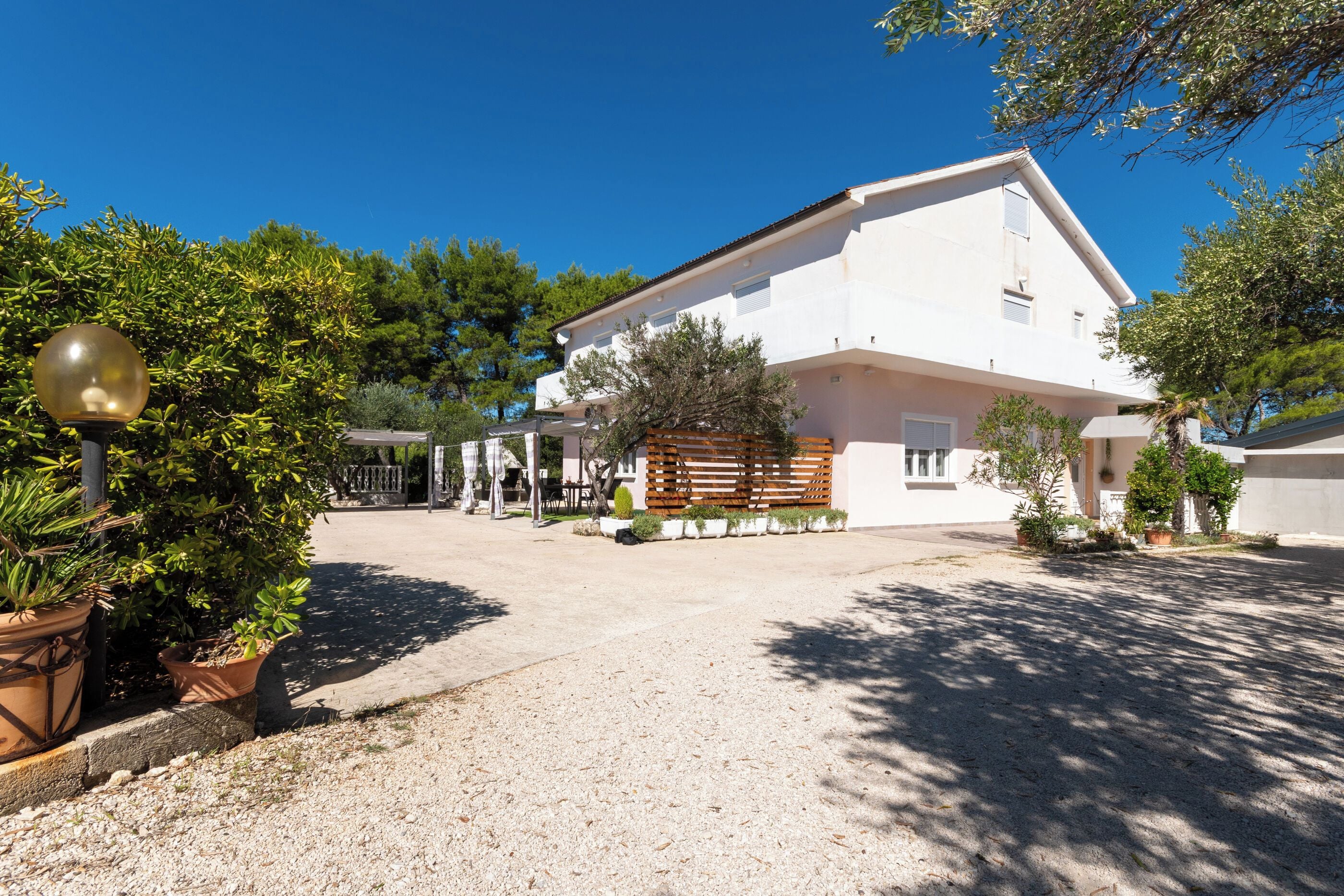 A white building with a gravel driveway, surrounded by greenery and trees.