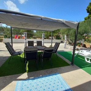 An outdoor patio with a table and chairs, a covered area, and artificial grass. - Apartment Buska (Vir)