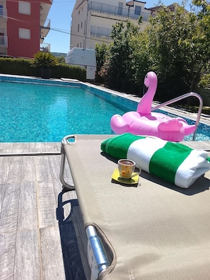 Una silla de descanso junto a la piscina, con una toalla, un flotador de flamenco rosa y una taza de café.