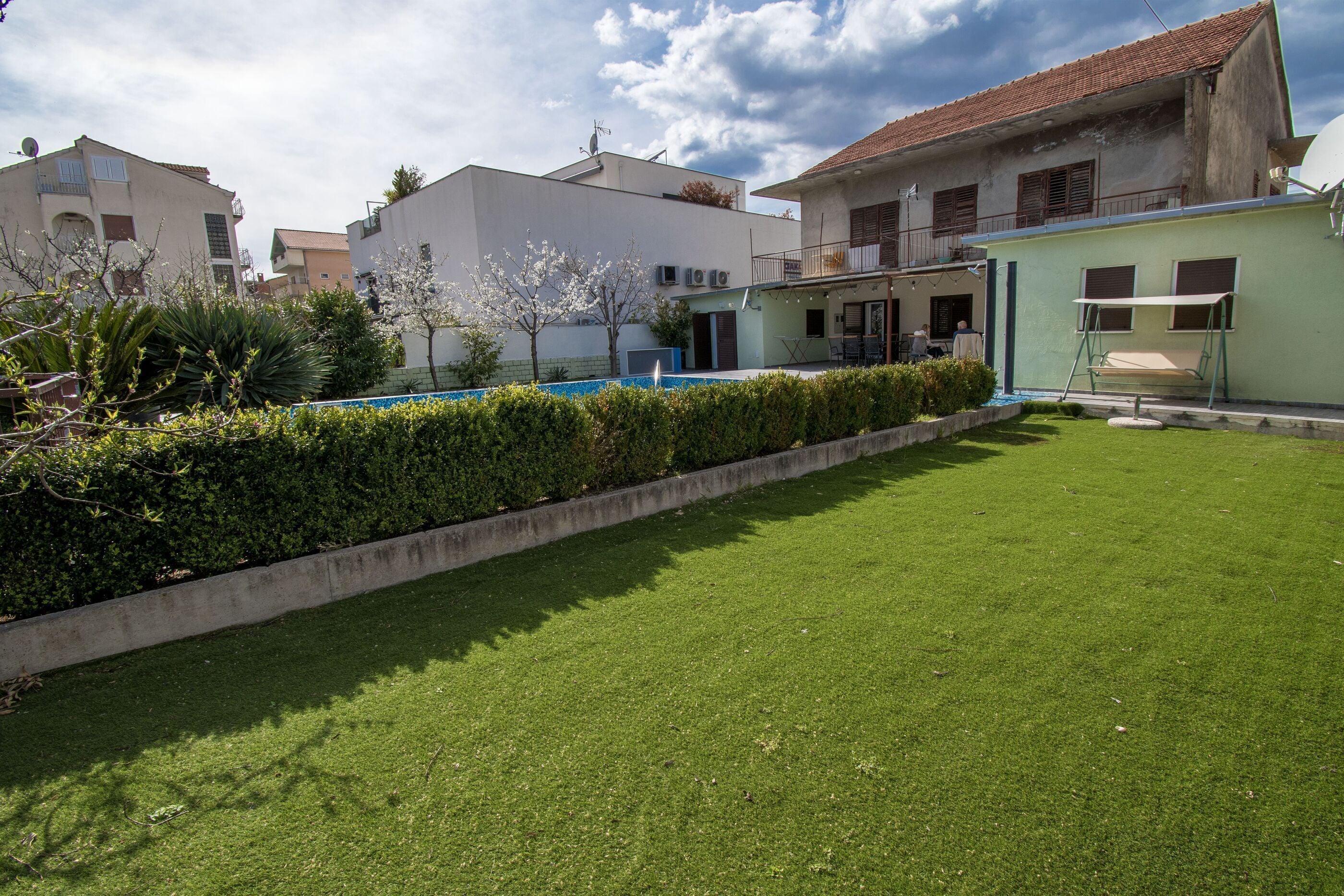 A residential area with a well-maintained lawn, a swimming pool, and a building with a balcony.