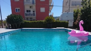 Ein Schwimmbecken mit einem rosa Flamingo-Schwimmtier, einem Teller mit Kirschen und einem Gebäude im Hintergrund.