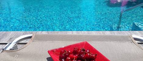 A swimming pool with a pink flamingo float, a red plate with cherries, and a building in the background.
