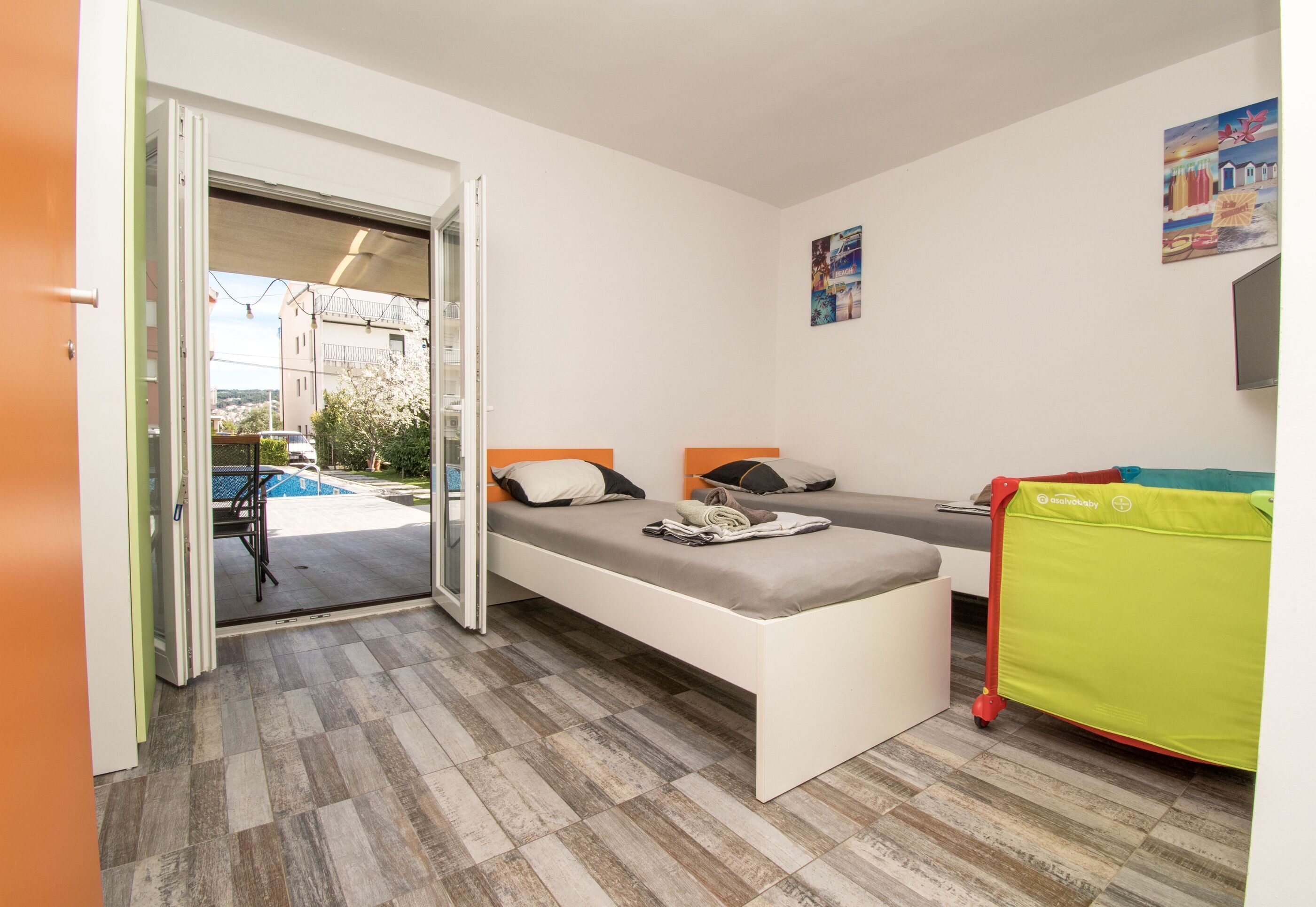 A room with two beds, a bench, a green chair, and a view of a swimming pool.