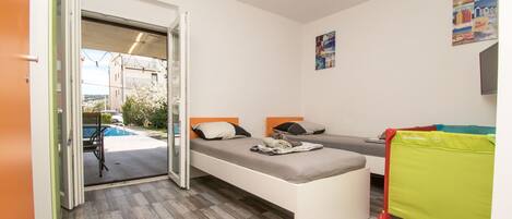 A room with two beds, a bench, a green chair, and a view of a swimming pool.