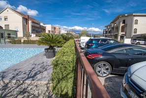Una calle residencial con coches aparcados, una piscina y casas con balcones.
