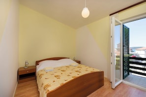Ein Schlafzimmer mit einem hölzernen Bett, einem Nachttisch, einer Lampe und einer Glastür zum Balkon.