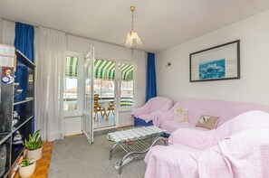 Ein Zimmer mit einem rosafarbenen Sofa, einem Glastisch mit Spielkarten, einem gerahmten Bild an der Wand und einem Fenster mit Vorhängen.