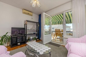 A living room with a TV, speakers, a glass coffee table, and a balcony with a striped awning. - Apartment Elvira Blue Beach (Vodice)